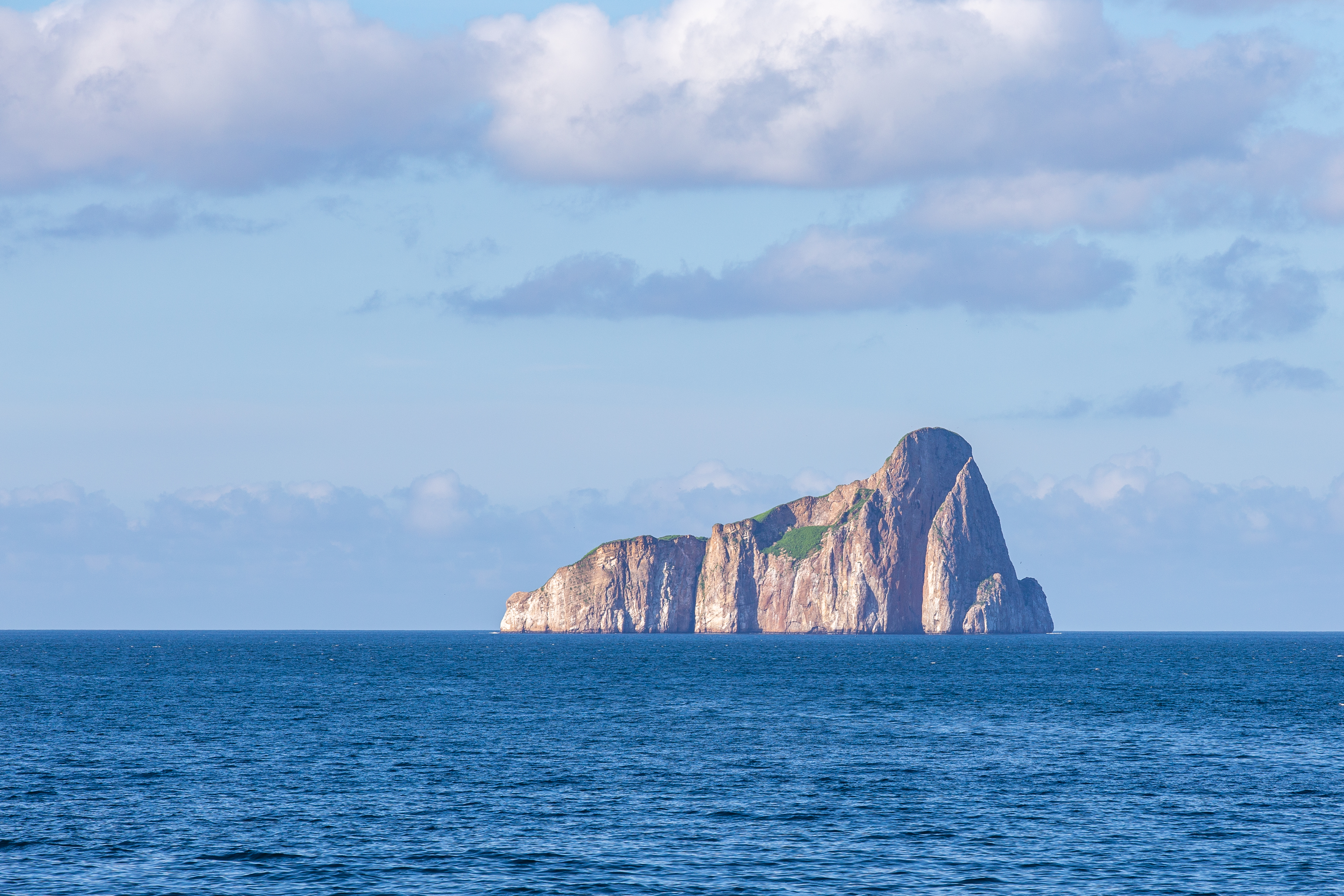 Kicker Rock rising from the open ocean under scattered clouds