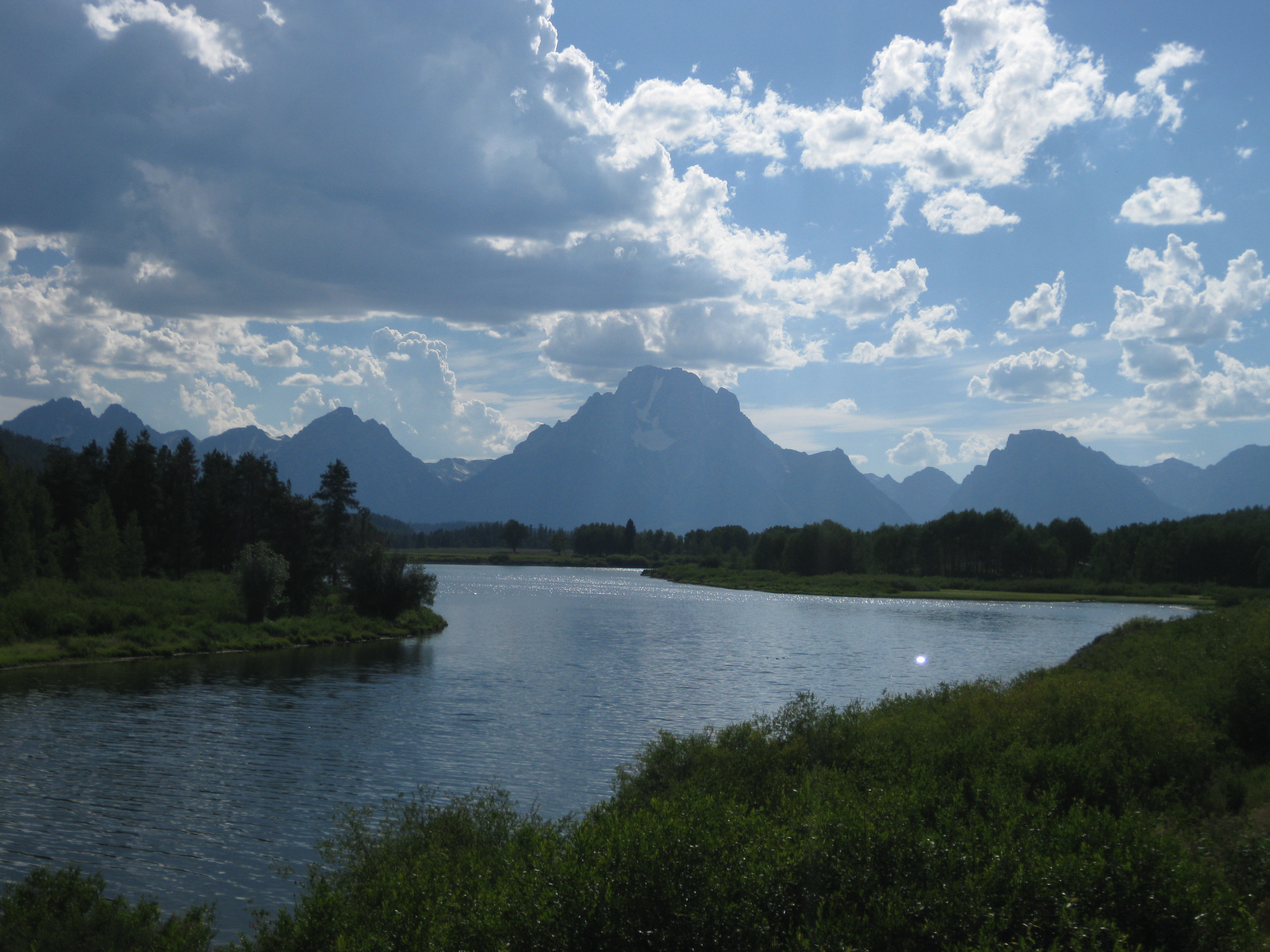 River curving through evergreen forest toward a mountain under a cloudy sky