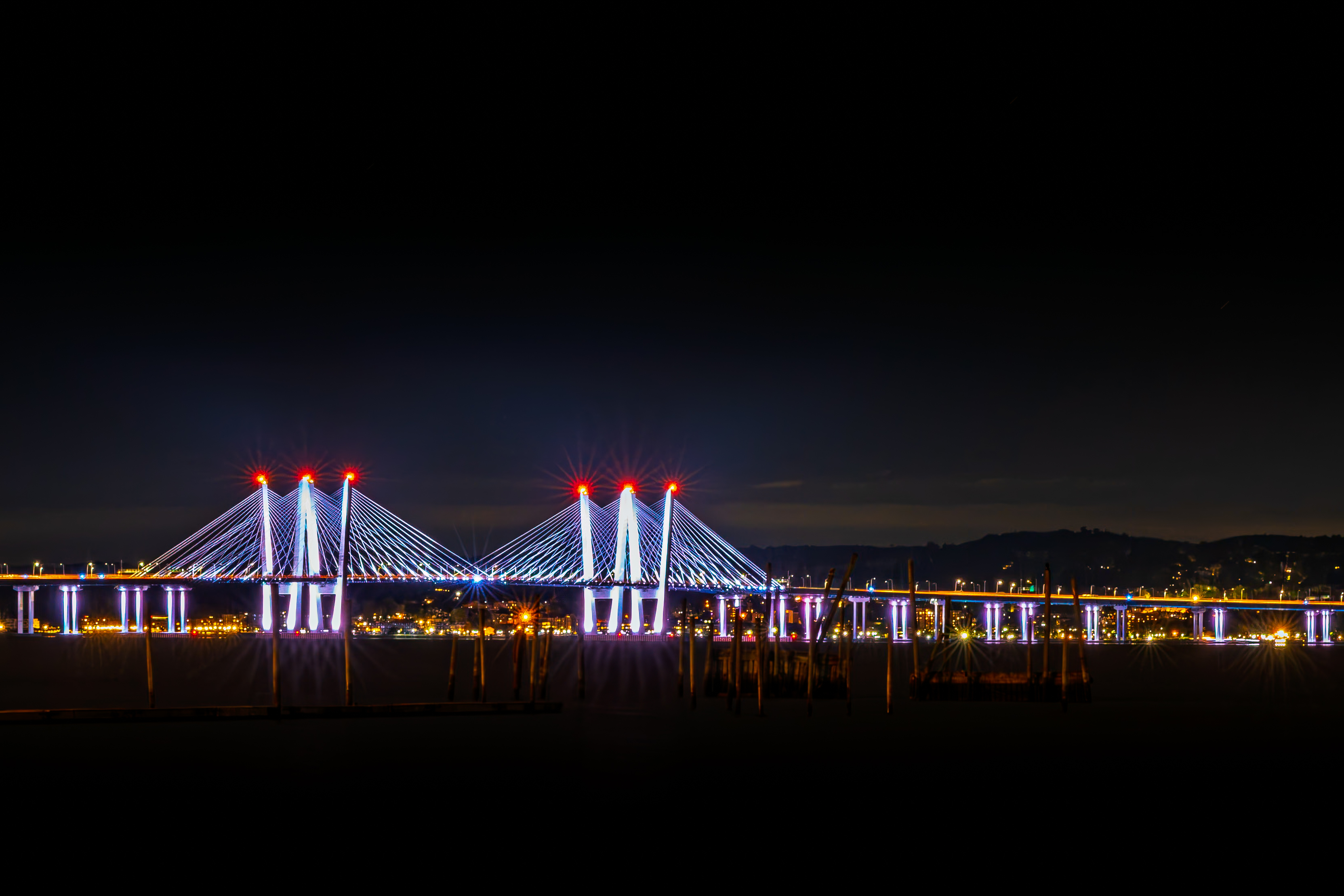 Cable-stayed bridge with white and purple lights against a black night sky